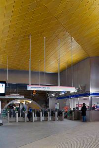 Anodised gold aluminium ceiling and shot-peened stainless steel cladding to ticket hall. Wood Lane underground station for London, Underground in partnership with Westfield - Architectural metalworks, platform seating, John Desmond Ltd. - Main contractor: Costain - Architect: Ian Ritchie architects - Principal engineer: Waterman Civils