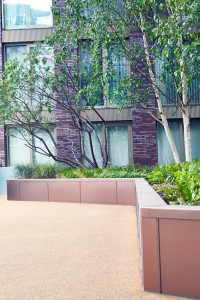 PVD coloured stainless steel in sandblasted Bronze, planters complementing the building materials. In shade the Bronze PVD has a cool tone. Embassy Gardens, London, UK.