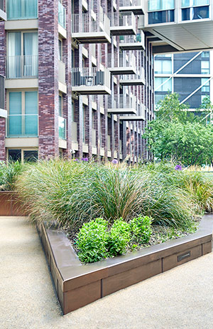 PVD coloured stainless steel in sandblasted Bronze, sharp angled corner section of planter. Embassy Gardens, London, UK. This image was taken in the shade and the Bronze shows as a cool tone.