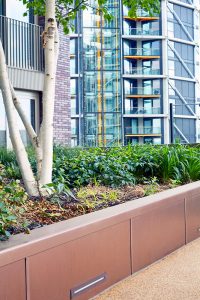 PVD coloured stainless steel in sandblasted Bronze which was specified to complement the green planting . Embassy Gardens, London, UK.