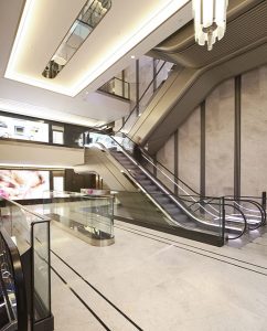 The renovated escalator hall with glossy new finishes and PVD coloured stainless steel trims. Architectural design by Make Architects PVD coloured stainless steel trim by John Desmond Ltd