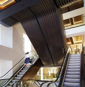 Escalators redolent of the Art Deco period with V-Grooved PVD stainless steel panels. - Architectural design by Make Architects. - PVD coloured stainless steel trim and panels by John Desmond Ltd.