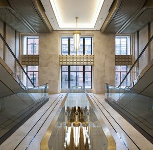 The renovated escalator hall in marble, glass, coated aluminium and PVD coloured stainless steel. Architectural design by Make Architects. PVD coloured stainless steel by John Desmond Ltd.