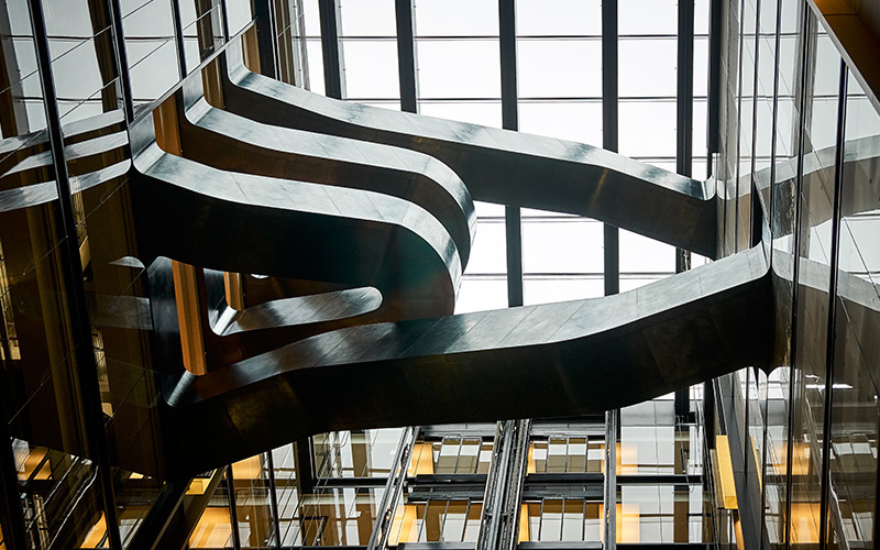 The staircase for Google, 6 Pancras Square, London, UK used blackened stainless steel with over-wax finish to create a sculptural feel. Showing view from below the stairs. Photography by Tim Soar.