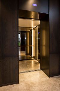 Architrave and panels in for elevator and lobby in V-Grooved PVD coloured stainless steel in Chocolate Vibration. - Fenman House, Apartment Building, 9 Handyside St, King’s Cross, London N1C. - Fabrication, V-Grooving and folding of PVD coloured stainless steel by John Desmond Ltd.