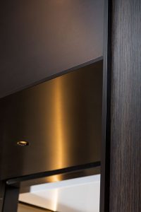 Close up view of elevator architrave and panels in V-Grooved PVD coloured stainless steel in Chocolate Vibration. - Fenman House, Apartment Building, 9 Handyside St, King’s Cross, London N1C. - V-Grooving and folding by John Desmond Ltd