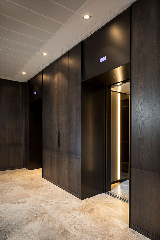 Elevator lobby with architrave and trim complementing the Wenge panelling and travertine floor. - Elevator architrave and panels in V-Grooved electro-zinc coated stainless steel. - Fenman House, Apartment Building, 9 Handyside St, King’s Cross, London N1C Manufacture by Bluecoat Engineering - Fabrication, V-Grooving and folding of stainless steel by John Desmond Ltd