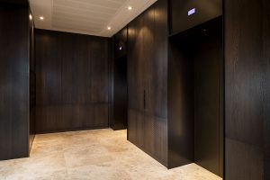 An upmarket look was required for this elevator lobby so dark, bronze-tones were specified which complement the travertine flooring. - Elevator architrave and panels in V-Grooved PVD coloured stainless steel in Chocolate Vibration. Fenman House, Apartment Building, 9 Handyside St, King’s Cross, London N1C. - Fabrication, V-Grooving and folding of stainless steel by John Desmond Ltd.