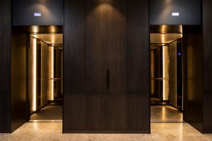 Warm lighting creates a welcoming lift cab interior. - Elevator architrave and panels in V-Grooved PVD coloured stainless steel in Chocolate Vibration. Fenman House, Apartment Building, 9 Handyside St, King’s Cross, London N1C. - Fabrication, V-Grooving and folding of stainless steel by John Desmond Ltd.