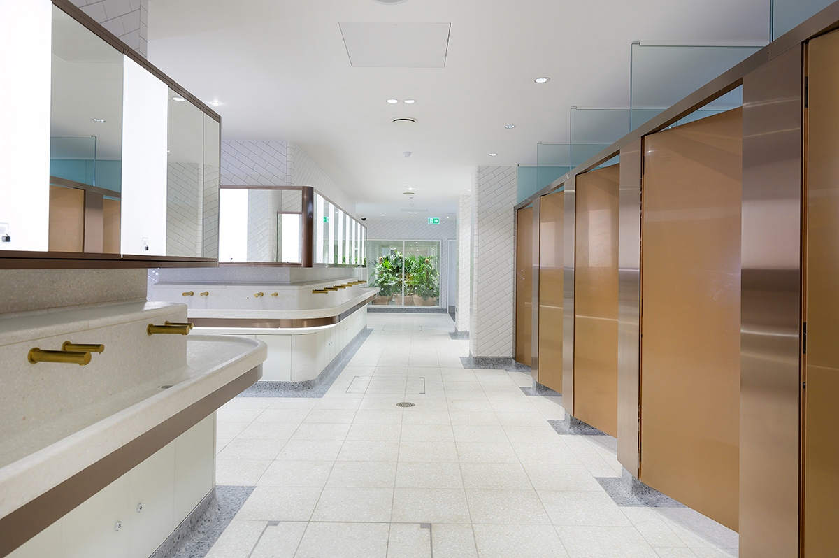 Visual for upgrade of WCs Victoria Station, London showing bronze PVD stainless steel taps and horizontal banding around communal basin.