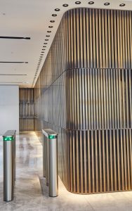 Narrow, stacked Bronze Brush PVD coloured stainless steel-clad bars with blackened ends create a feature wall at the rear of the reception area. - 1 Broadgate Quarter, Snowden St, London, EC2A 2AW - Architects: John Robertson Architects.