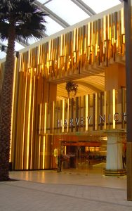 Undulating façade, columns and detailing in Double Stone Steel PVD coloured stainless steel Royal Gold Mirror. - Harvey Nichols retail department store, The Avenues, Kuwait. - Client: Four IV Interior Design - Architect: Gensler - Developer: Mabanee
