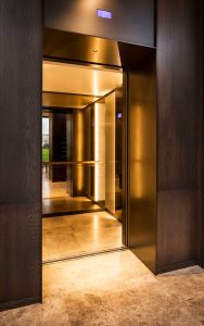 Elevator lobby with door skins, overhead panel and architrave in V-Grooved PVD coloured stainless steel Chocolate Vibration. - Fenman House, Apartment Building, 9 Handyside St, King’s Cross, London N1C 4AY. - Building design: Maccreanor Lavington Architects - Interiors: Johnson Naylor Architects - Developer: Argent - Fabrication, V-Grooving and folding of stainless steel: John Desmond Ltd.