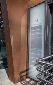 Tapered column in Chocolate PVD stainless steel V-Grooved and folded to appear as solid bronze. Fabricated and installed by John Desmond Ltd. - Office building, 15 Fetter Lane, EC4A, London. - Architects: McBains Cooper - Client: British Steel Pension Fund Trustees Ltd - Fit-out: Nucom Interiors
