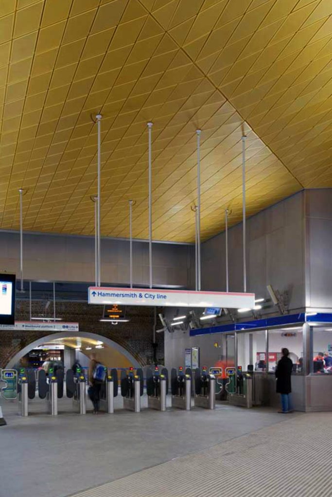 Showing the gold, or brass-coloured,  anodised aluminium diagonally-set ceiling panels to the Wood Lane Underground Station, London. Architectural design by Ian Ritchie Architects. Ceiling by John Desmond Ltd.