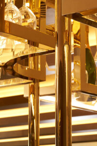 Detail of overhead bar rack in Champagne Mirror PVD coloured stainless steel which has been V-Grooved and folded to appear as solid brass.