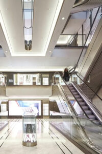 Escalators redolent of the Art Deco period with V-Grooved PVD stainless steel panels. - Architectural design by Make Architects. - Stainless steel trim and panels fabricated by John Desmond Ltd.